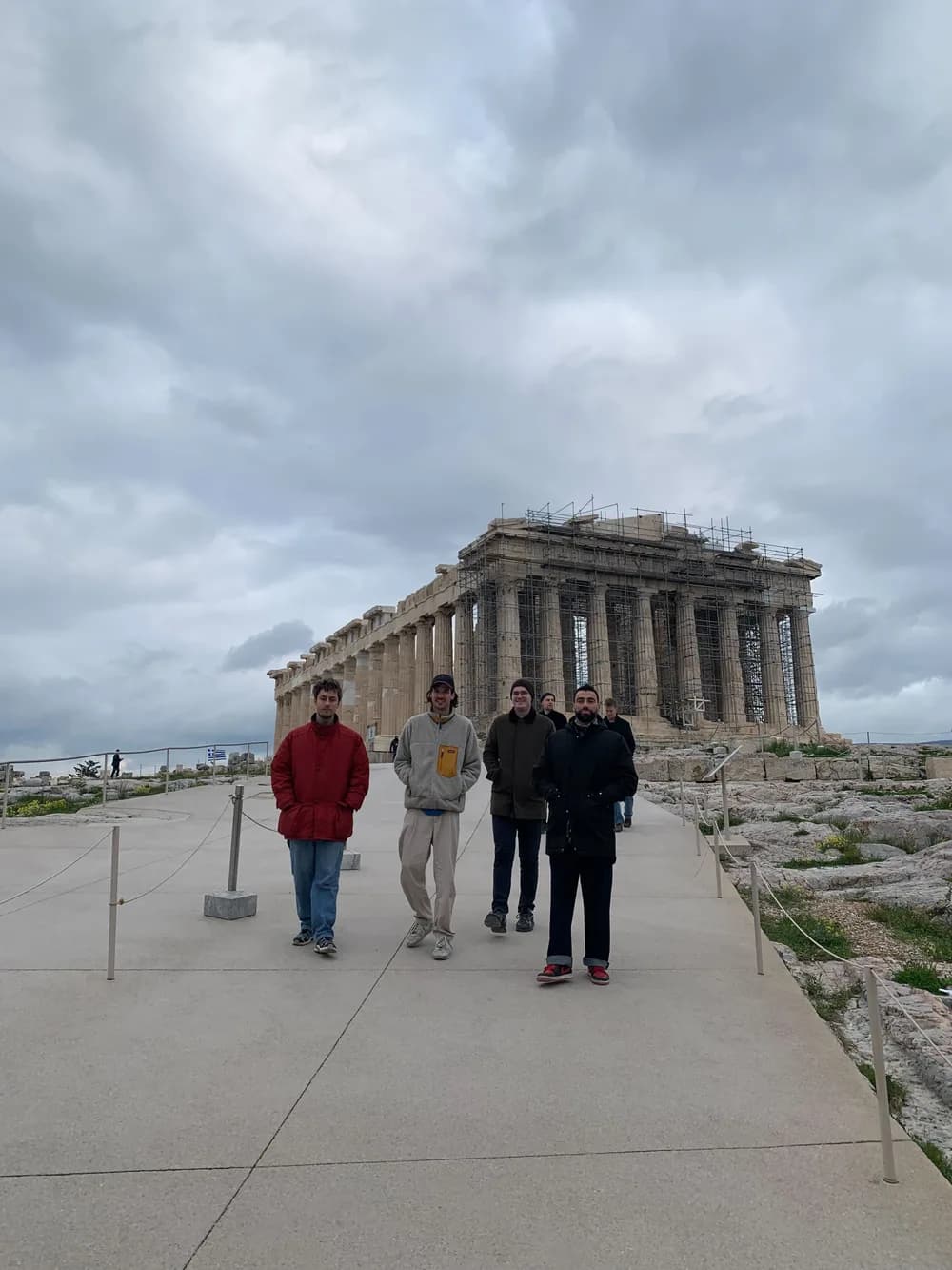 Four people standing in front of the Parthenon in Athens beneath an overcast sky.